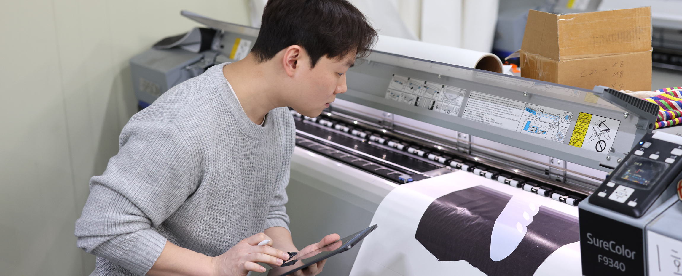 담당자가 상품이 정확히 제작되고 있는지 기계와 상품을 교차 확인하며 태블릿에 특이사항을 기재하는 모습